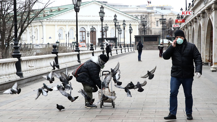 Женщина в респираторе кормит птиц на Манежной площади в Москве, 30 марта 2020 года