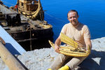 Юрий Сенкевич, врач, член интернационального экипажа папирусной лодки «Ра-2», с макетом лодки в руках. На заднем плане — папирусная лодка, 1970 год