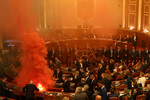 Депутат Демократической партии, крупнейшей оппозиционной партии Албании, зажигает цветную дымовую шашку в знак протеста во время сессии парламента в Тиране, Албания, 20 ноября 2023 года