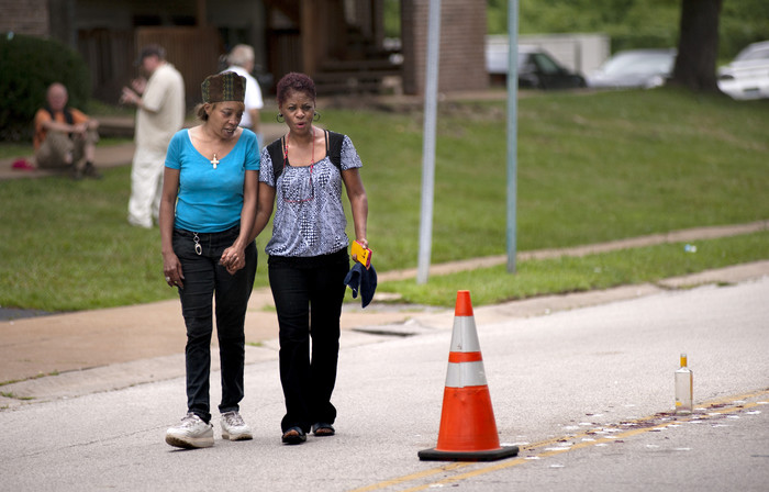 Женщины держат друг друга за&nbsp;руку, осматривая место, где был застрелен полицией Майкл Браун