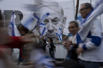 Протестующие против судебной реформы Израиля идут с национальными флагами Израиля рядом с транспарантом, на котором изображен премьер-министр Биньямин Нетаньяху, Тель-Авив, Израиль, 25 марта 2023 года