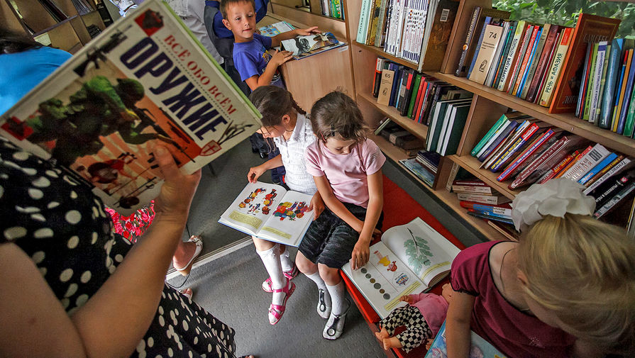 Школьники читают книги в автобусе передвижной библиотеки во дворе школы на хуторе Клетском Волгоградской области.