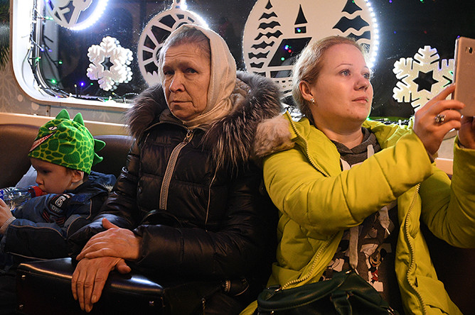 Пассажиры в новогоднем поезде московского метро, украшенном гирляндами и еловыми ветками