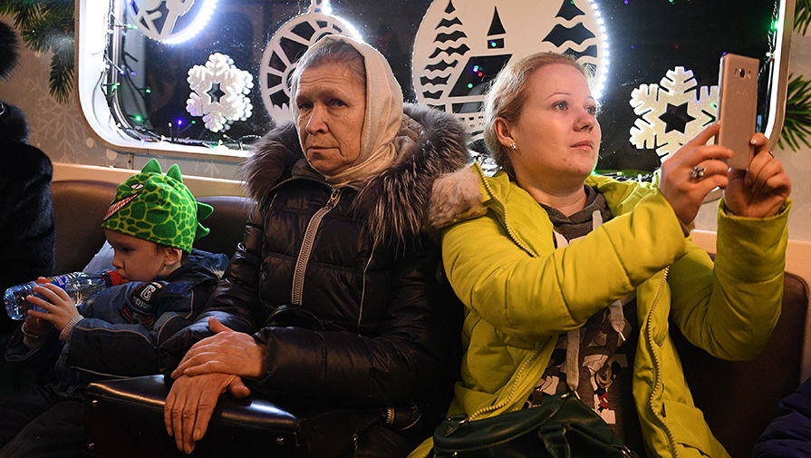 Пассажиры в&nbsp;новогоднем поезде московского метро, украшенном гирляндами и еловыми ветками