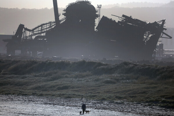 Мужчина выгуливает собак на&nbsp;фоне частично разрушенной доменной печи бывшего сталелитейного завода в&nbsp;Редкаре, Великобритания, 30&nbsp;января 2023&nbsp;года