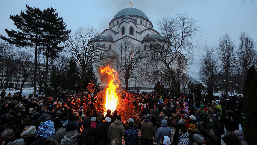 Верующие сжигают сухие ветви дуба, который символизирует Святочный Йоль, на Православное Рождество в передней части храма Святого Саввы в Белграде, Сербия